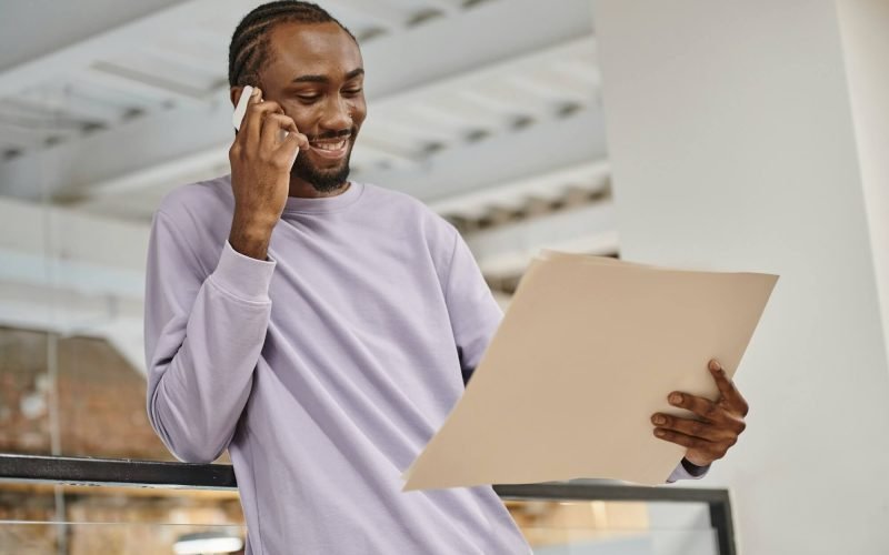 happy-african-american-man-looking-at-project-on-paper-talking-on-smartphone-planning-startup.jpg